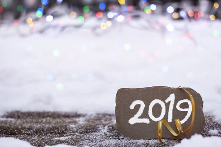 Brown piece of cardboard with the inscription 2019 on the background of snow and bright lightsの写真素材