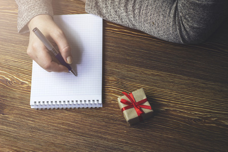 A woman makes a note in a notebook that lies on a wooden table next to the gift boxの写真素材