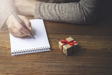 A woman makes a note in a notebook that lies on a wooden table next to the gift boxの写真素材