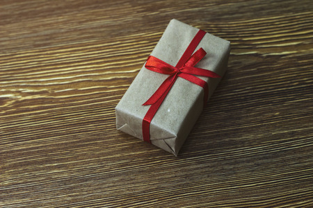 A gift box with a red ribbon is on a wooden table