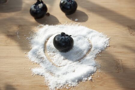 blueberry in the middle of a heart formed with sugar-free granules along with some unfocused fruits, arranged on a wooden kitchen boardの写真素材