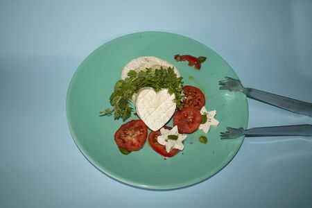 Brie cheese cut in the shape of a heart accompanied by basil leaves and flowers, slices of tomato...