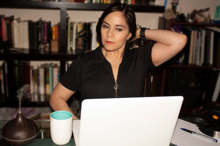 Woman working at home office with a large bookcase behind her using laptop computer on a glass table while the pleasant smelling humidifier in its steam smells the environmentの写真素材