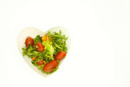 Lettuce mixed with red cherry tomatoes in a heart-shaped bowl organic vegan foodの写真素材