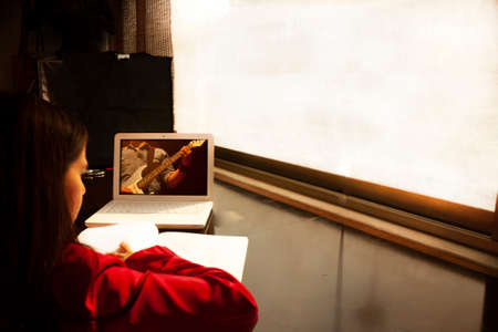 Woman with notebook in hand connected to video call from home with guitar teacher in Mexico City