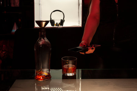 Person making payment at the bar counter for a drink of Whiskey on the rocks using mobile device...