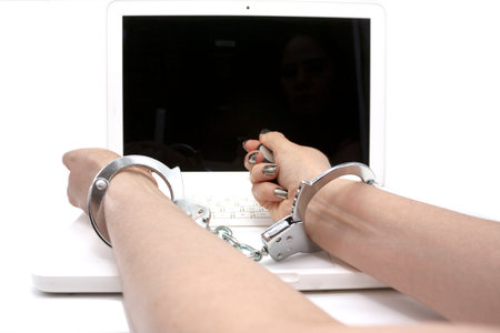 Outstretched arm of a woman with handcuffs to wrists on computer roof conceptual cyber crimeの写真素材