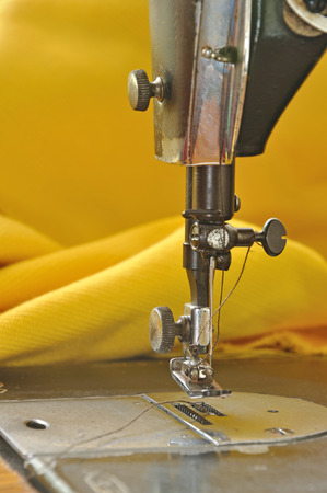 old  sewing machine foot with yellow fabric backgroundの写真素材