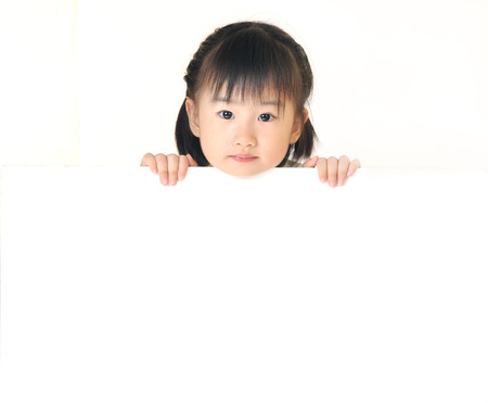 Asian little girl hiding behind a blank white board and peeks over the toの写真素材