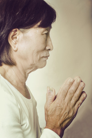 old asian buddhist woman praying with her hands put togetherの写真素材