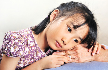 Asian little girl leaning her head on senior hand or her grandmother hand. Human family love. の写真素材
