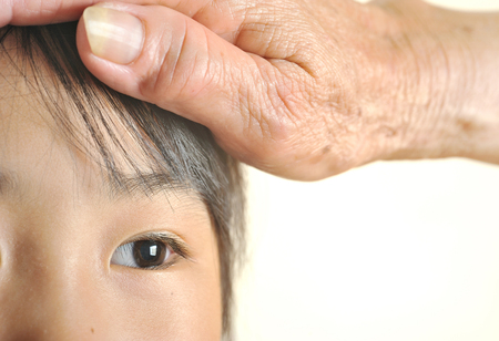 children eye closeup selective focus with her grandmother care. Happy asian eye little girl with wrinkle hand senior strokes her head. Human family love. の写真素材