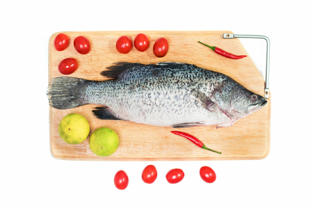 Fresh raw Asian Sea Bass fish  on wooden cutting board with lemon, tomato and chilli on white background, top view. Seafood asian cooking ingredients.の写真素材