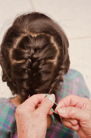 Closeup of head of asian kid. Grandmother is making of braids on little granddaughter's. selective...