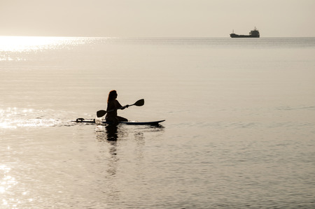 Woman silhouette  on windsurf board and tanker against sunset sea backgroundの写真素材