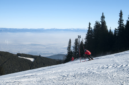 Ski slope with skiers descending on background of winter mountain landscape in clear sunny dayの写真素材