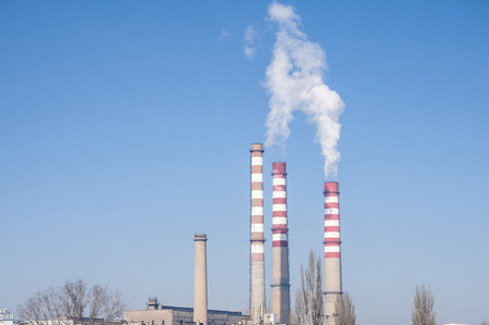Smoking chimneys of thermal power plant on clear blue sky background