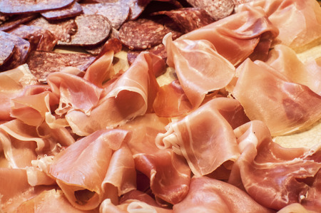 Sliced dry sausages and prosciutto as appetizer closeup as background