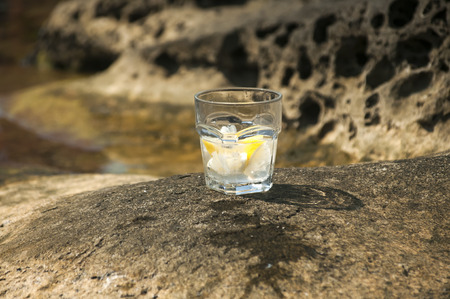 Glass with ice drink on sea cliff amid quiet summer seaの写真素材