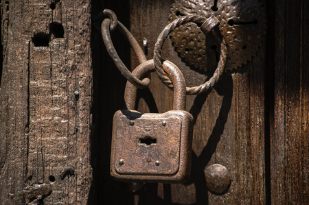 Old weathered grunge rusty locked padlock with rings on old wooden board doorの写真素材