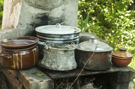 Outdoor fireplace in rural yard with stacks of old metal pots and clay cookwareの写真素材
