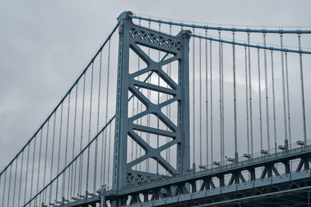 Large blue painted vintage iron suspension bridge over big river in cloudy day