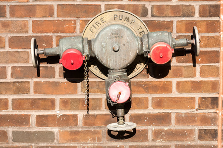 Fire hydrant with tree valves mounted on red brick house wallの写真素材