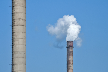 Obsolete vintage industrial chimneys with white smoke on blue sky backgroundの写真素材