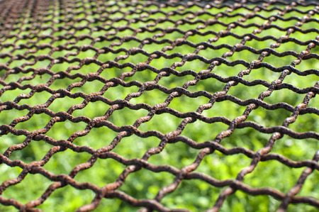 Weathered grunge old rusty wire fencing net closeup on green grassy backgroundの写真素材