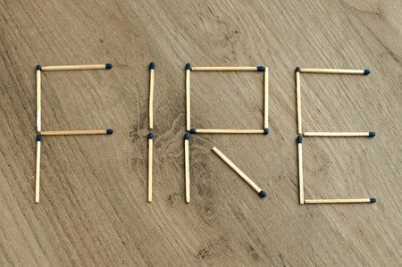 The word "fire" written by wooden matchsticks on wooden board backgroundの写真素材