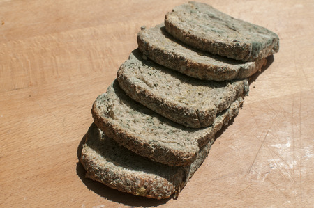 Moldy slices of whole-grain bread closeup on wooden board backgroundの写真素材
