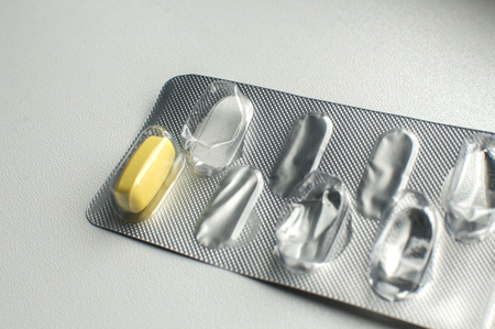 One yellow pill left in used empty medicine blister pack closeup on white background