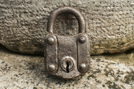 Old weathered grunge retro locked padlock closeup on solid stone surface background