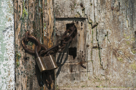 Old locked retro padlock and iron chain of grunge wooden rural door closeupの写真素材