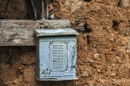 Old weathered grunge obsolete metal tin post letter box on adobe clay wall of abandoned rural country house closeupの写真素材