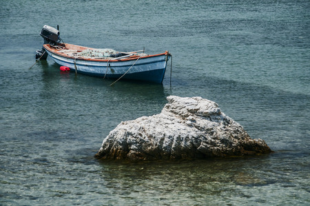Fishing boat anchored in calm blue sea waters near sea rock in sunny summer day