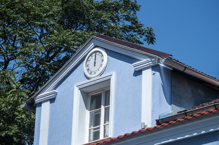Top of blue painted old vintage house with white wall clock under the roofの写真素材