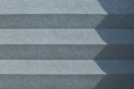 Folded textile window blind lit by sunlight closeup as backgroundの写真素材