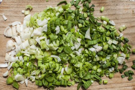 Fresh green onions chopped, sliced and prepared to cook on wooden cutting board closeup as food...