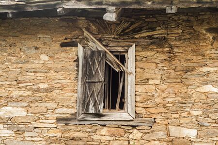 Grunge wooden window on abandoned rural house stone wall closeupの写真素材
