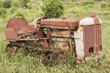 Old neglected rusty small vintage caterpillar tractor on green meadowの写真素材
