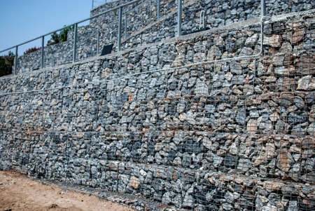 Galvanized gabion mesh stone wall closeup in summer day