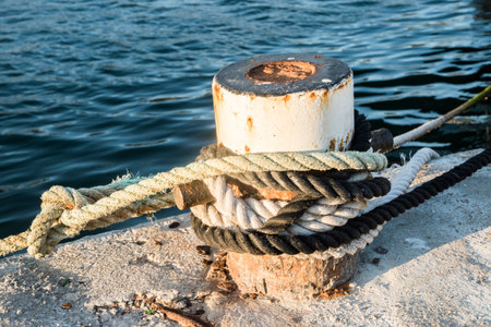 Old metal dock mooring pole with rope for securing fishing boats closeup