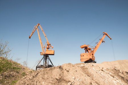 Industrial landscape with cranes in the sand against the blue sky. Port industrial cranes at river sand unloading depot on clear sunny dayの写真素材