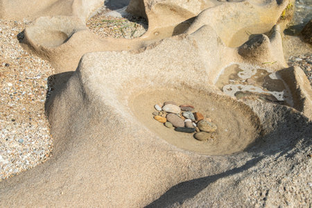 A beautiful sandstone rock eroded by the sea with a water-filled depression and pebbles closeup