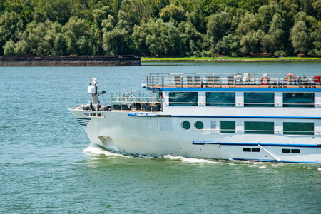The bow of a large passenger river cruise ship sailing calmly on the river's surface on a clear dayの写真素材