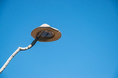 A straw sun hat perched comically on a tall wooden stick against a bright, clear blue sky