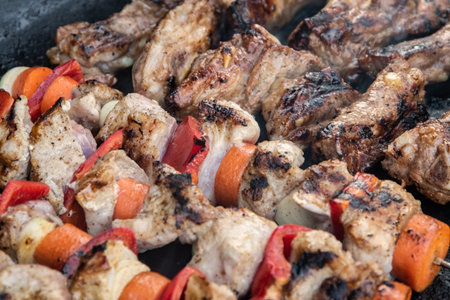 Raw pork skewers and grilled ribs cooking side by side on a hot barbecue grill, close-up view
