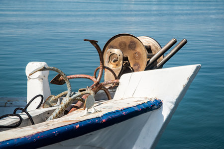 Old wooden fishing boat bow with vintage mechanical reels docked on a calm blue sea