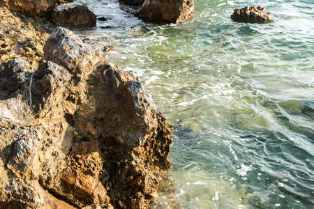 Crystal clear Mediterranean waters gently wash rugged seaside rocks under a bright summer sunの写真素材